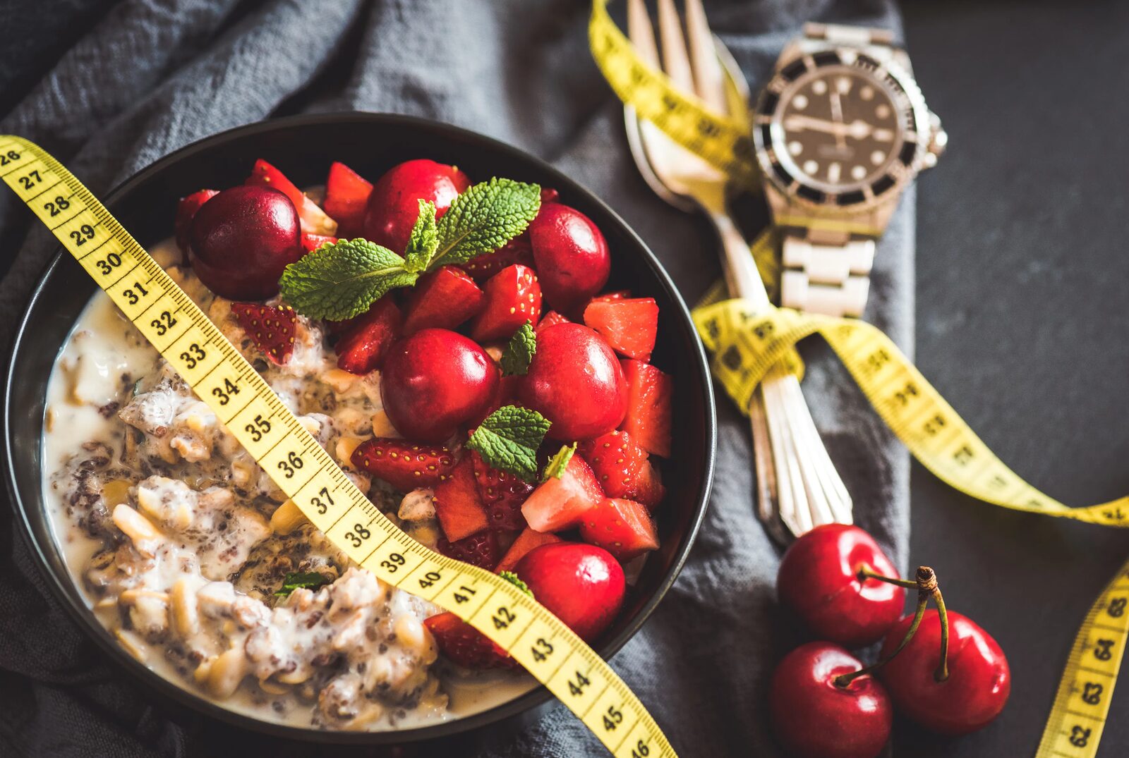 A bowl of oats and berries beside a tape measure on a dark surface